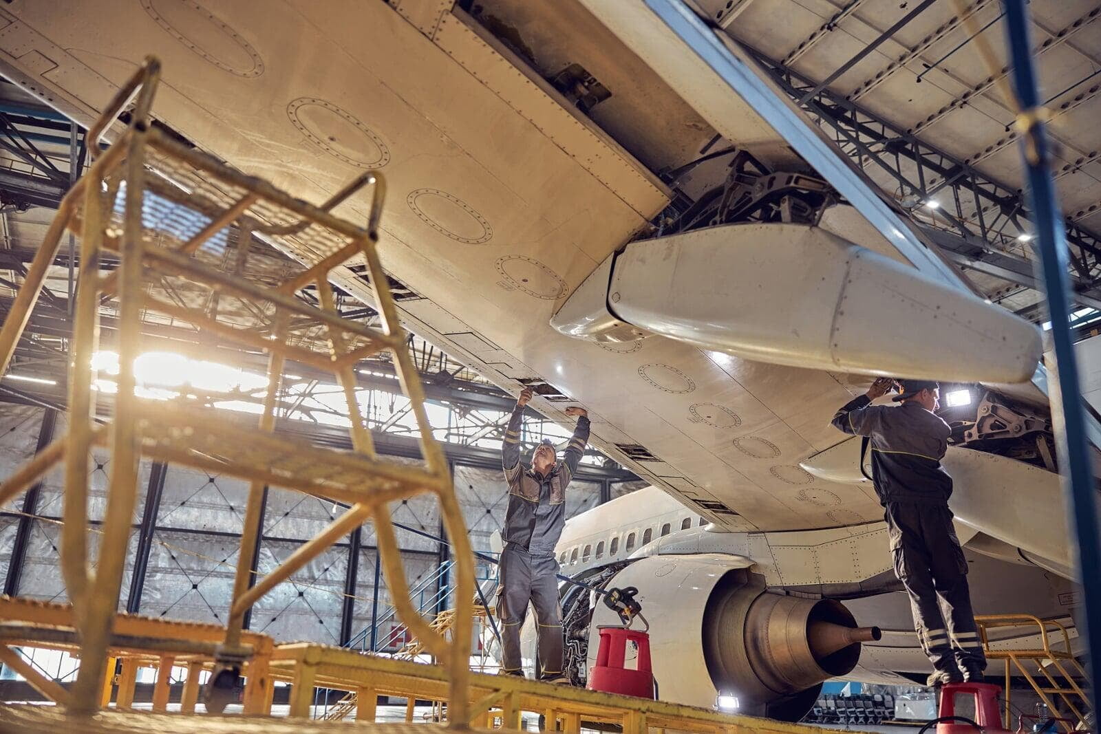 Two workers are working under an airplane wing.